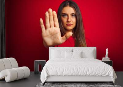 Young beautiful woman wearing t-shirt standing over isolated red background doing stop sing with palm of the hand. Warning expression with negative and serious gesture on the face. Wall mural