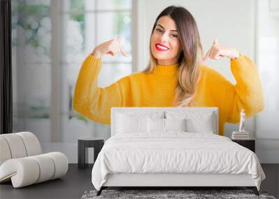 Young beautiful woman wearing winter sweater at home looking confident with smile on face, pointing oneself with fingers proud and happy. Wall mural