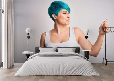 Young beautiful woman with blue fashion hair wearing casual t-shirt over white background Looking proud, smiling doing thumbs up gesture to the side Wall mural