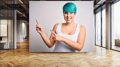 Young beautiful woman with blue fashion hair wearing casual t-shirt over white background smiling and looking at the camera pointing with two hands and fingers to the side. Wall mural