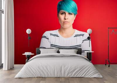 Young beautiful woman with blue fashion hair wearing striped sweater over red background skeptic and nervous, disapproving expression on face with crossed arms. Negative person. Wall mural