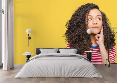 Young beautiful woman with curly hair wearing stripes t-shirt with hand on chin thinking about question, pensive expression. Smiling with thoughtful face. Doubt concept. Wall mural