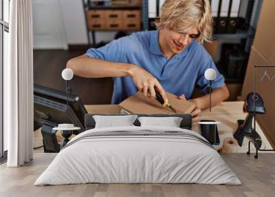 Young blond man ecommerce business worker unpacking cardboard box at office Wall mural