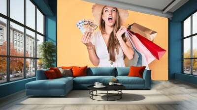 Young blonde girl holding shopping bags and canadian dollars angry and mad screaming frustrated and furious, shouting with anger looking up. Wall mural