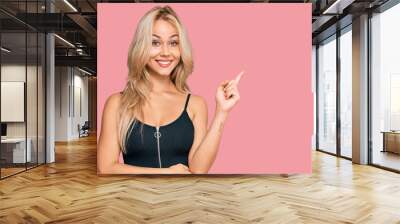 Young blonde girl wearing elegant and sexy look smiling happy pointing with hand and finger to the side Wall mural