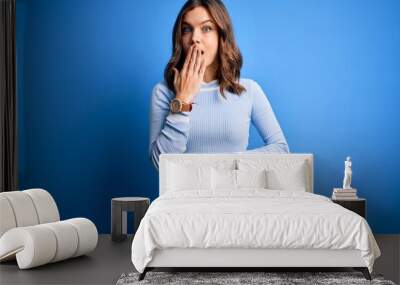 Young blonde slim girl holding measuring tape on body waist over blue background cover mouth with hand shocked with shame for mistake, expression of fear, scared in silence, secret concept Wall mural