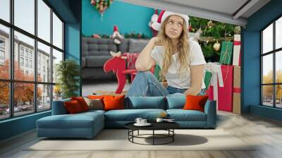 Young blonde woman celebrating christmas sitting on floor with sad expression at home Wall mural