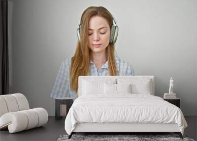 Young blonde woman listening to music using headphones and smartphone over isolated white background Wall mural