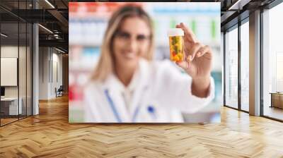 Young blonde woman pharmacist smiling confident holding pills bottle at pharmacy Wall mural