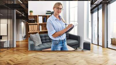 Young blonde woman psychologist writing on clipboard standing at clinic Wall mural