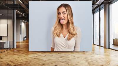 Young blonde woman standing over isolated background sticking tongue out happy with funny expression. emotion concept. Wall mural