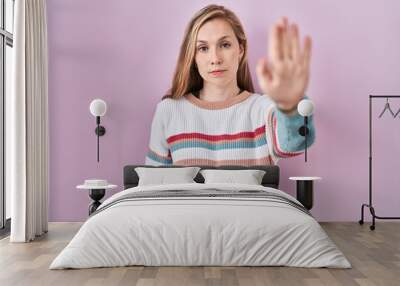 Young blonde woman standing over pink background doing stop sing with palm of the hand. warning expression with negative and serious gesture on the face. Wall mural