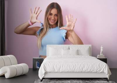 Young blonde woman standing over pink background showing and pointing up with fingers number ten while smiling confident and happy. Wall mural