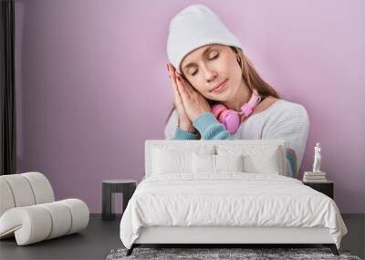 Young blonde woman standing over pink background sleeping tired dreaming and posing with hands together while smiling with closed eyes. Wall mural