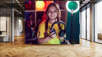 Young blonde woman streamer smiling confident holding headphones at gaming room Wall mural