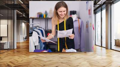 Young blonde woman tailor smiling confident looking clothing design at tailor shop Wall mural