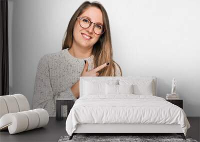 Young blonde woman wearing casual sweater and glasses cheerful with a smile of face pointing with hand and finger up to the side with happy and natural expression on face Wall mural