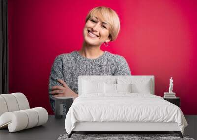 Young blonde woman with modern short hair wearing casual sweater over pink background happy face smiling with crossed arms looking at the camera. Positive person. Wall mural