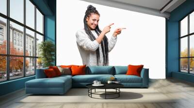 Young braided hair african american girl wearing sweater over isolated background smiling and looking at the camera pointing with two hands and fingers to the side. Wall mural