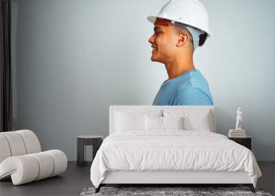 Young brazilian engineer man wearing security helmet standing over isolated white background looking to side, relax profile pose with natural face with confident smile. Wall mural