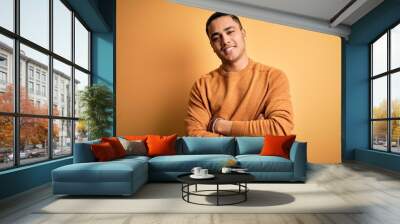 Young brazilian man wearing casual sweater standing over isolated yellow background happy face smiling with crossed arms looking at the camera. Positive person. Wall mural