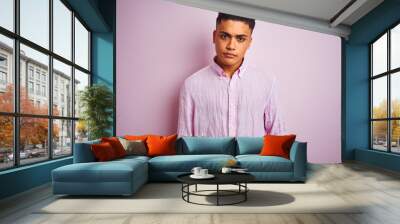 Young brazilian man wearing shirt standing over isolated pink background Relaxed with serious expression on face. Simple and natural looking at the camera. Wall mural