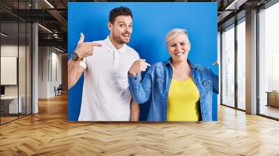 Young brazilian mother and son standing over blue background looking confident with smile on face, pointing oneself with fingers proud and happy. Wall mural