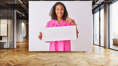 Young brazilian nurse woman holding banner standing over isolated white background very happy pointing with hand and finger Wall mural