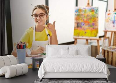 Young brunette teenager at art studio smiling doing phone gesture with hand and fingers like talking on the telephone. communicating concepts. Wall mural