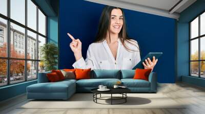 Young brunette teenager using touchpad device smiling happy pointing with hand and finger to the side Wall mural