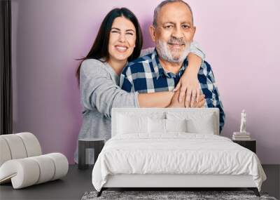 Young brunette woman and senior man standing over pink background. Daughter and father hugging and bonding together as happy family Wall mural