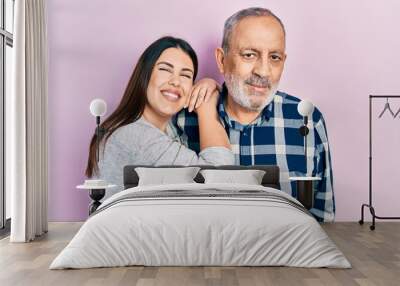 Young brunette woman and senior man standing over pink background. Daughter and father hugging and bonding together as happy family Wall mural