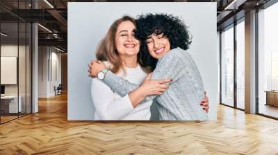 Young brunette woman and senior woman standing over isolated background. Daughter and mother hugging and bonding together as happy family Wall mural