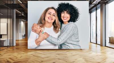 Young brunette woman and senior woman standing over isolated background. Daughter and mother hugging and bonding together as happy family Wall mural