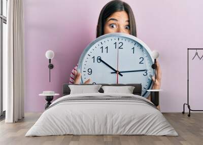 Young brunette woman holding big clock covering face celebrating crazy and amazed for success with open eyes screaming excited. Wall mural