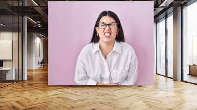 Young brunette woman standing over pink background with hand on stomach because nausea, painful disease feeling unwell. ache concept. Wall mural