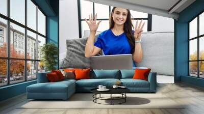 Young brunette woman using laptop at home showing and pointing up with fingers number eight while smiling confident and happy. Wall mural