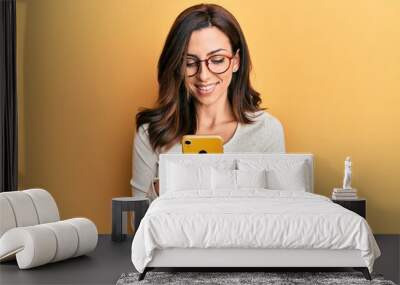 Young brunette woman using smartphone over yellow background smiling with a happy and cool smile on face. showing teeth. Wall mural