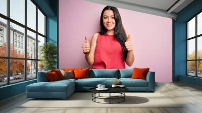 Young brunette woman wearing casual summer shirt over pink isolated background success sign doing positive gesture with hand, thumbs up smiling and happy. Cheerful expression and winner gesture. Wall mural