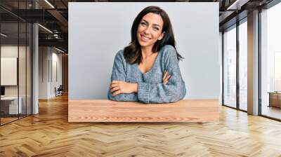 Young brunette woman wearing casual sweater sitting on the table happy face smiling with crossed arms looking at the camera. positive person. Wall mural