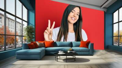 Young brunette woman wearing casual white tshirt over red background showing and pointing up with fingers number two while smiling confident and happy. Wall mural