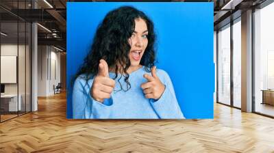 Young brunette woman with curly hair wearing casual clothes pointing fingers to camera with happy and funny face. good energy and vibes. Wall mural