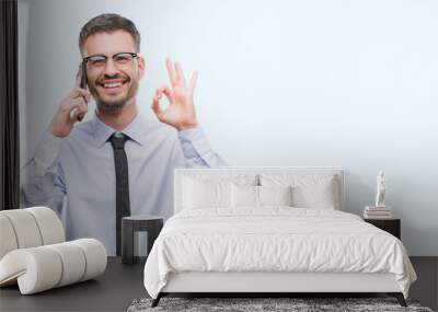 Young business adult man talking on the phone doing ok sign with fingers, excellent symbol Wall mural