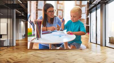 Young caucasian child playing at playschool with teacher. Mother and son at playroom drawing a draw with color pencils Wall mural