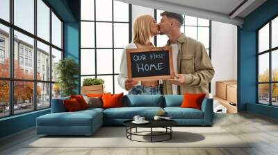 Young caucasian couple kissing and holding blackboard with our first home message at new house Wall mural