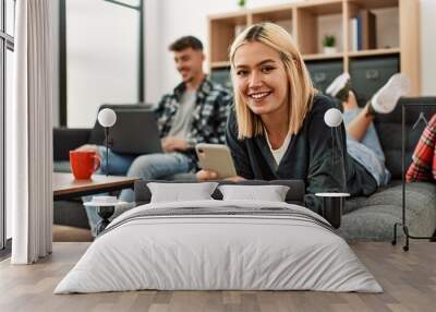 Young caucasian couple smiling happy using laptop and smartphone sitting on the sofa at home. Wall mural