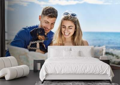 Young caucasian couple standing with dog looking map at the beach. Wall mural