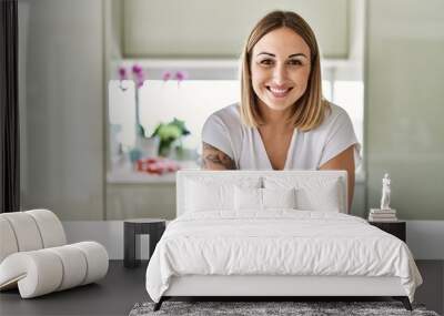 Young caucasian girl smiling happy leaning on the table standing at the kitchen. Wall mural