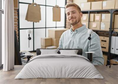 Young caucasian man ecommerce business worker sitting on table smiling at office Wall mural