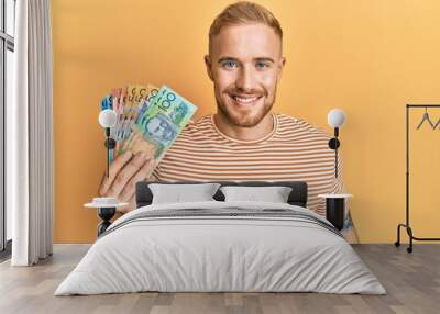 Young caucasian man holding australian dollars looking positive and happy standing and smiling with a confident smile showing teeth Wall mural